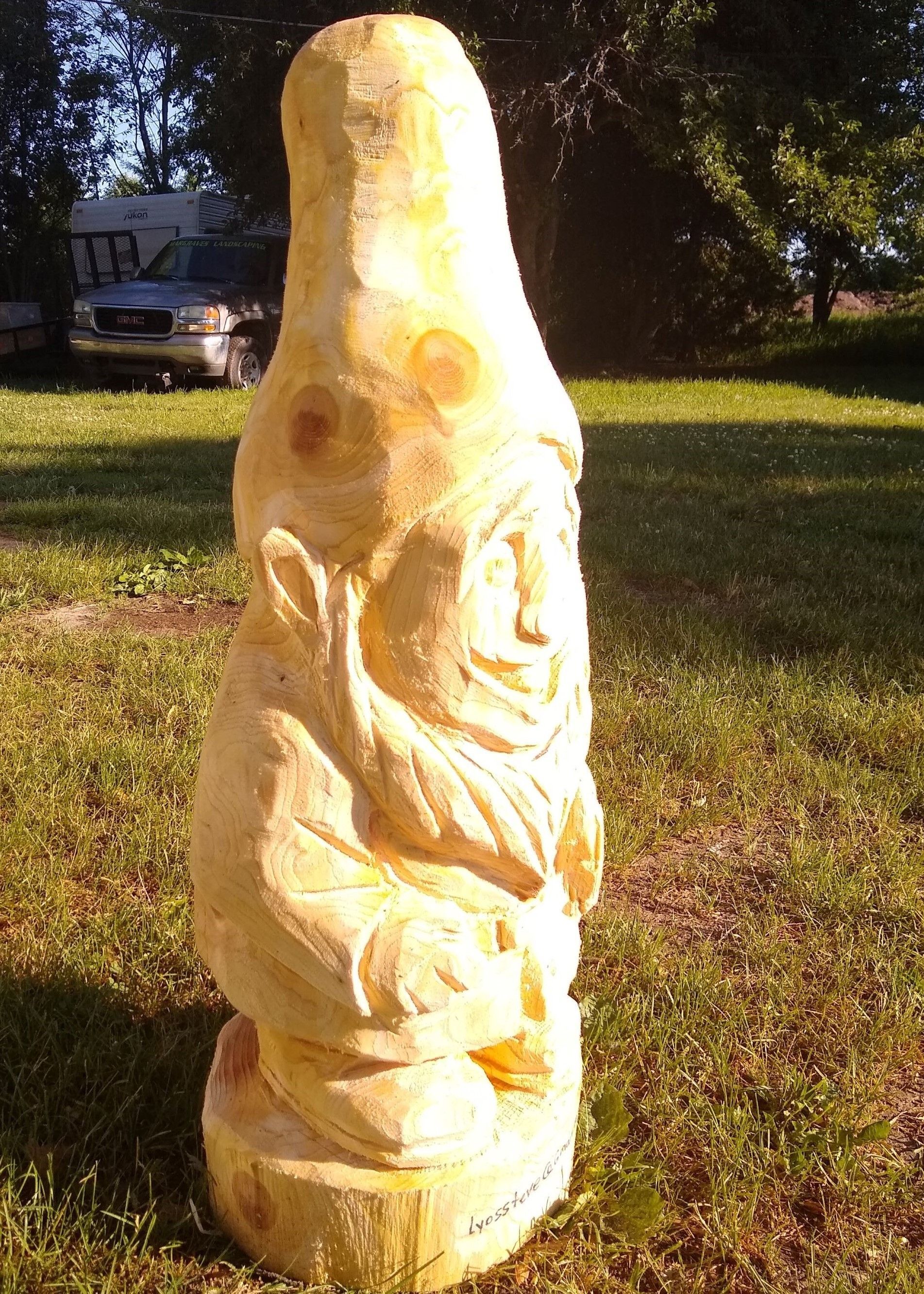 Carved stone sculpture with a yellowish finish standing on grass in a sunny yard