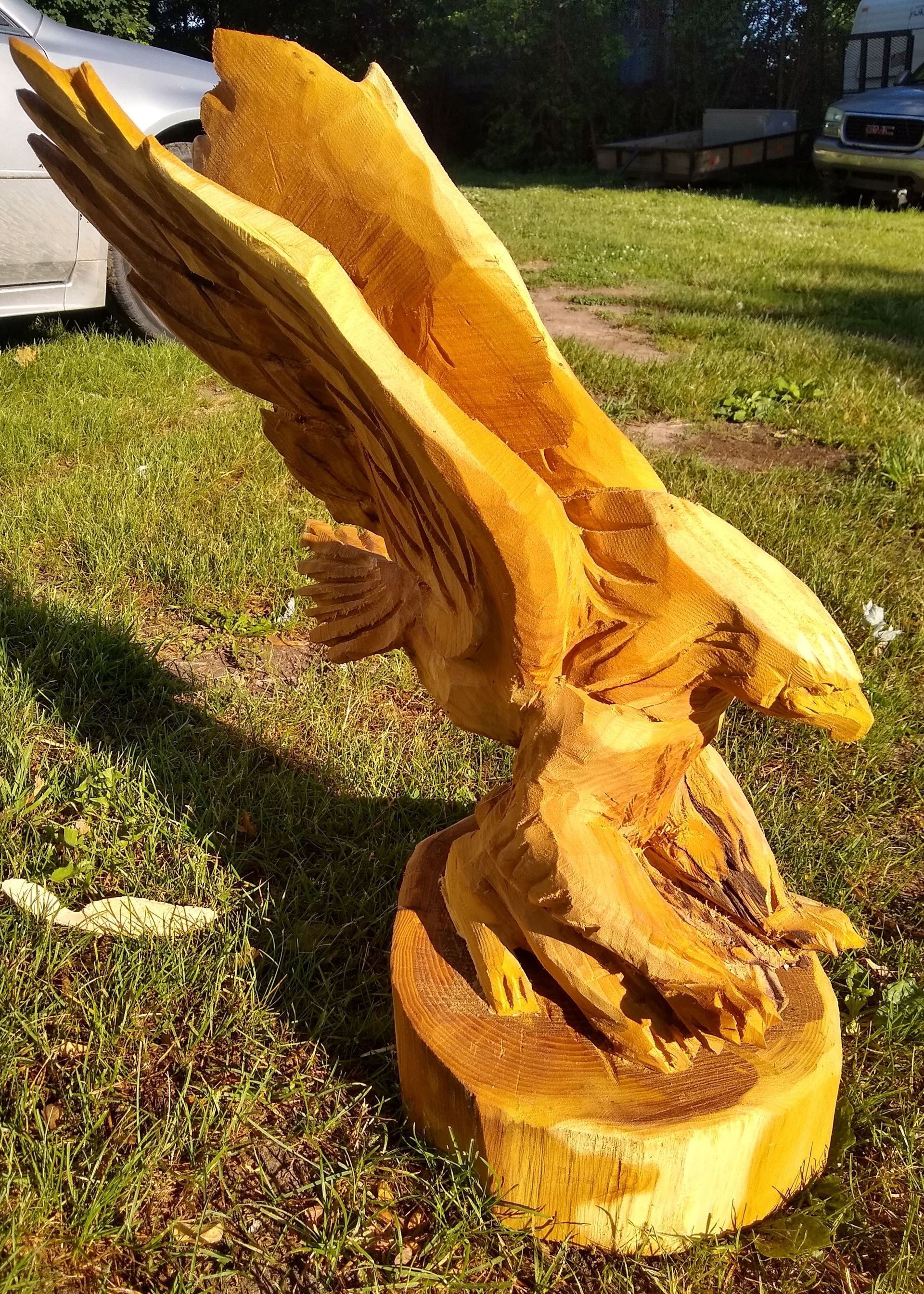 Carved wooden eagle sculpture on a tree stump in a grassy yard, wings spread wide.