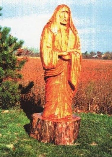 Wooden statue of a robed figure standing on a stump in a grassy field