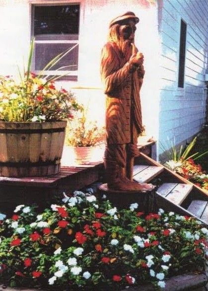 Bronze dog statue beside flower bed and potted plants next to a house porch