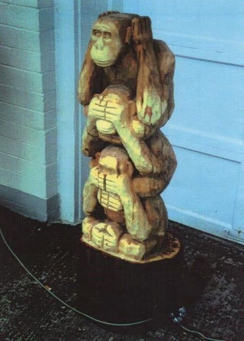 Wooden carved monkey statue by a blue wall on a dark floor