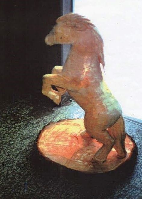 Wooden horse figurine standing on a round base, lit from the side against a dark background