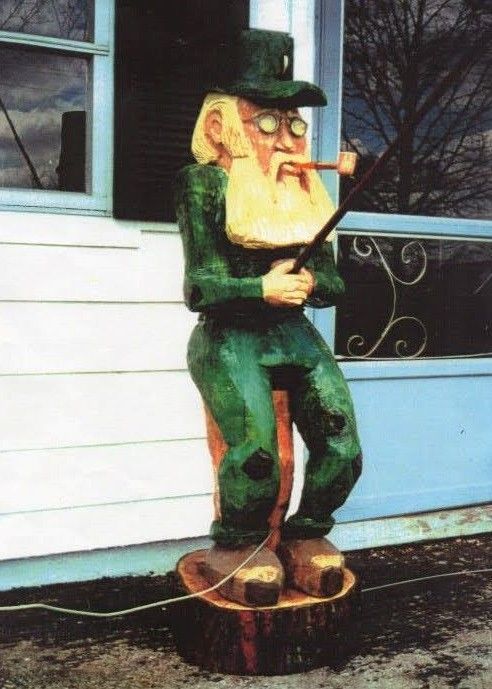 Wooden statue of a cigar-smoking fisherman in green clothes standing by a porch railing