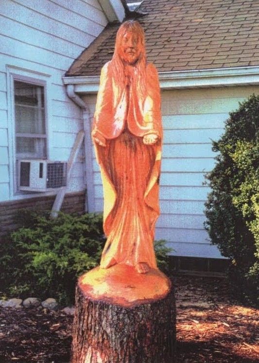 Wooden carved statue standing on a tree stump in a yard beside a house