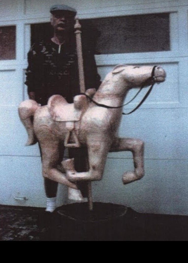 Man standing behind a white wooden rocking horse on a pole in front of a garage door
