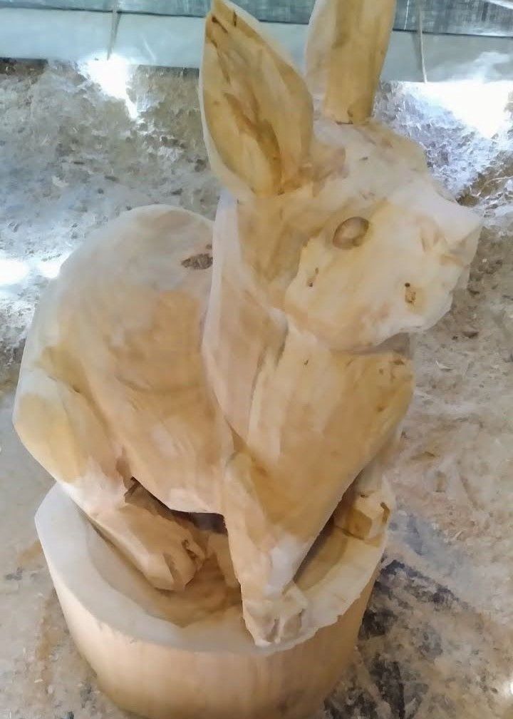 Wooden rabbit sculpture on a round base, carved in light tan wood on a stone surface.