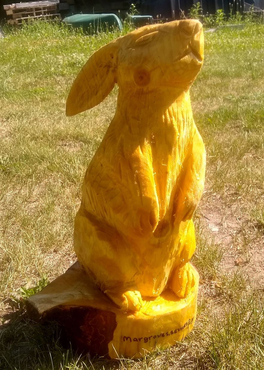 Yellow cat statue in a grassy yard, sitting upright in sunlight