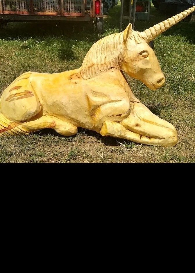 Yellow unicorn statue lying on grass, with a long horn and folded legs
