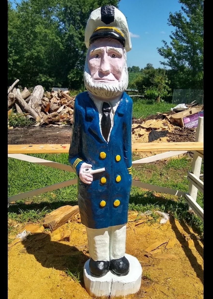Wooden sailor statue in a blue coat and white hat standing outdoors on a sunny day