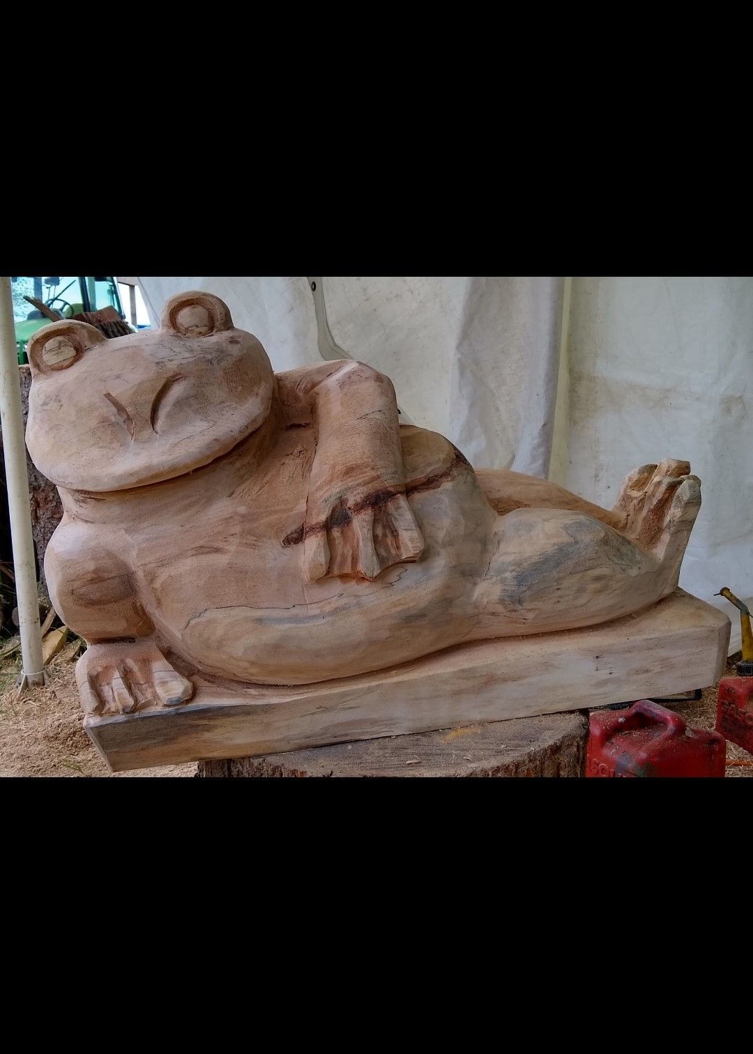 Reclining tan clay sculpture of a smiling figure on a base with one hand raised and feet resting on the edge