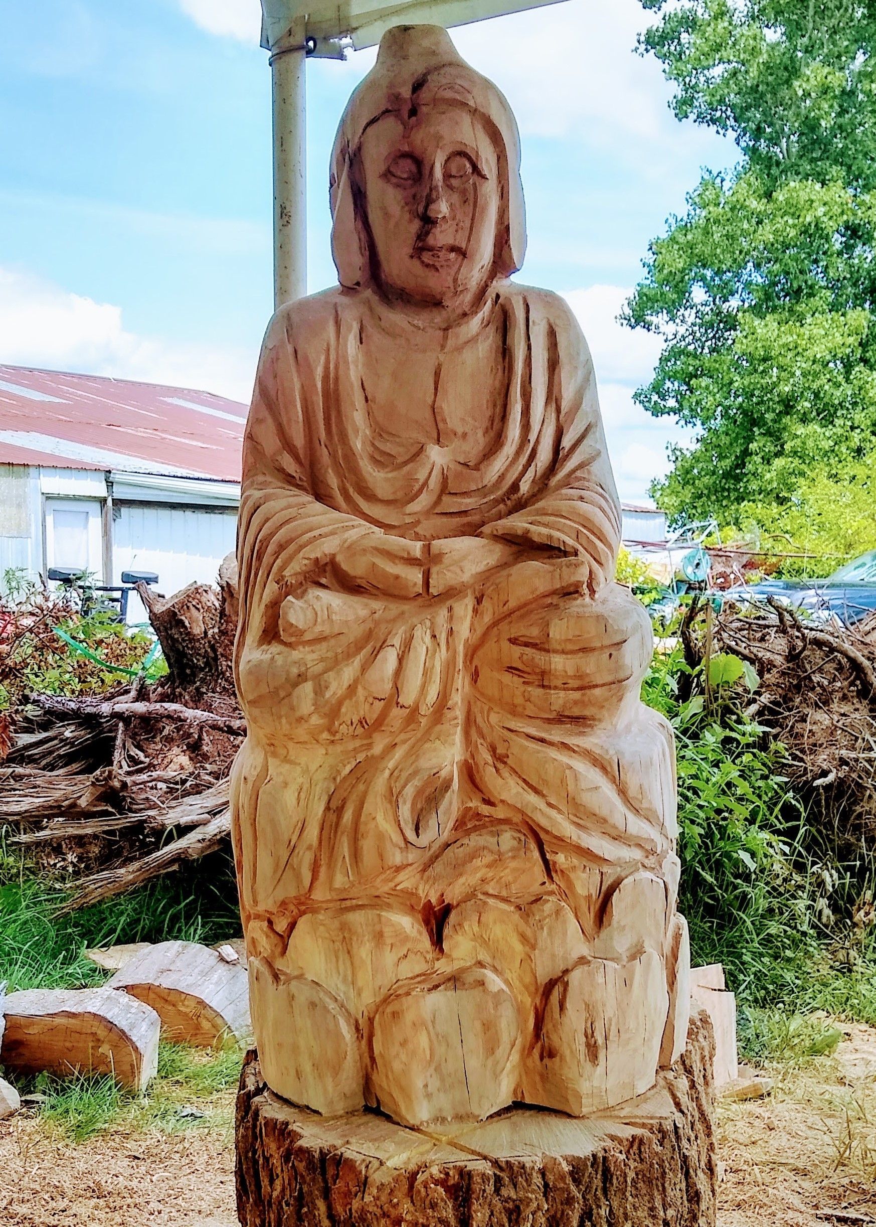 Wooden seated statue outdoors with trees and a blue sky in the background