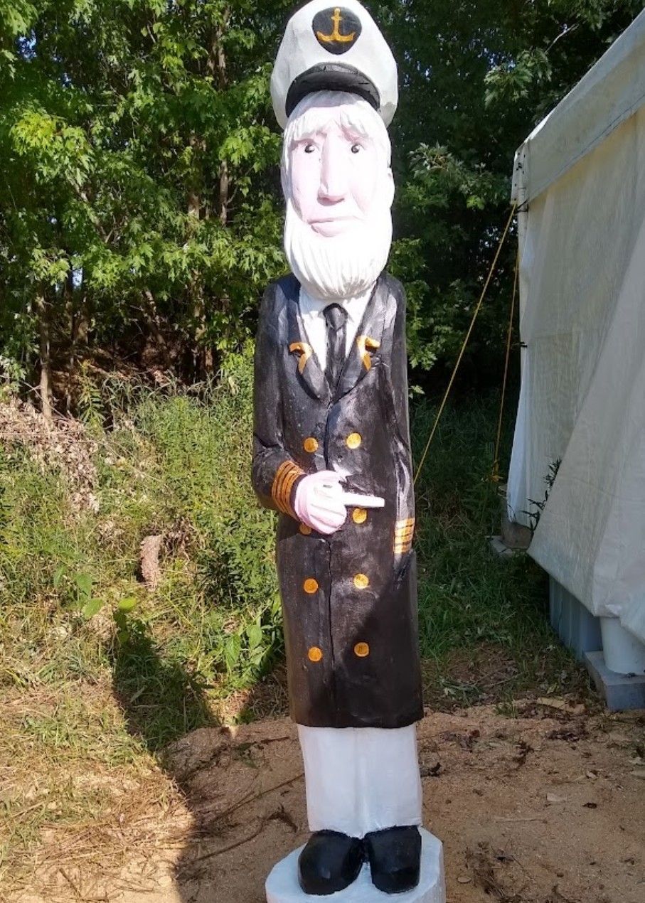 Statue of a captain in a dark navy coat and hat standing outdoors beside a white tent.