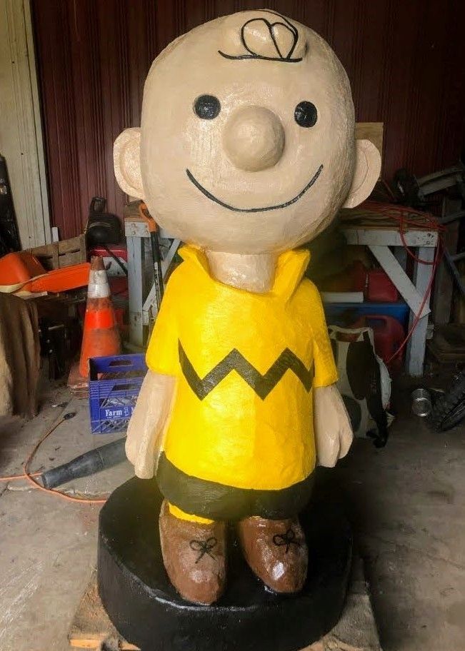 Cartoon statue of Charlie Brown in a yellow shirt and black shorts, standing indoors on a black base.
