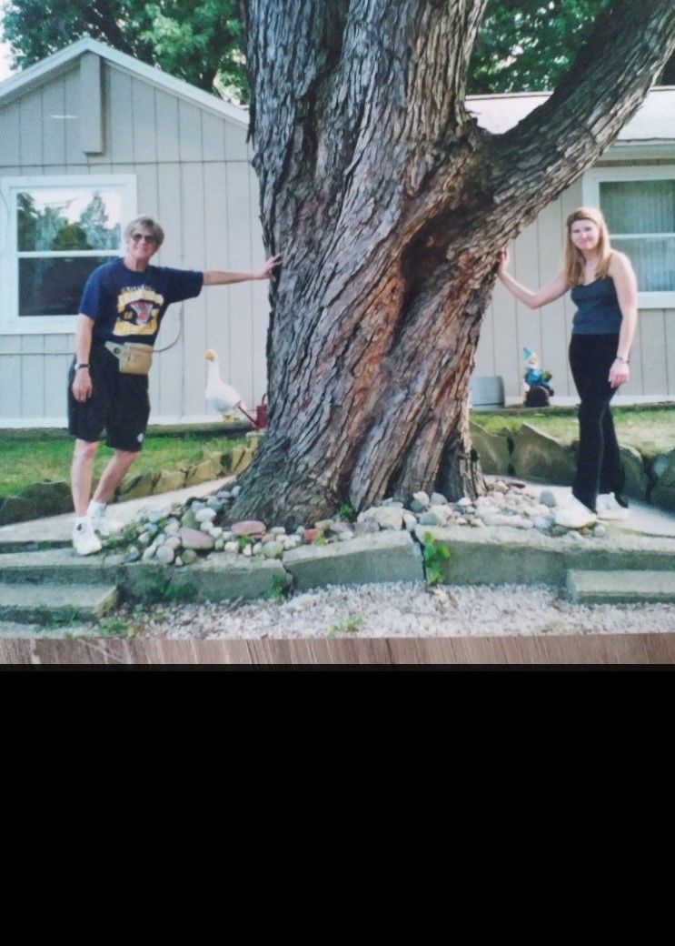 Three people standing beside a large carved wooden statue outside a building.