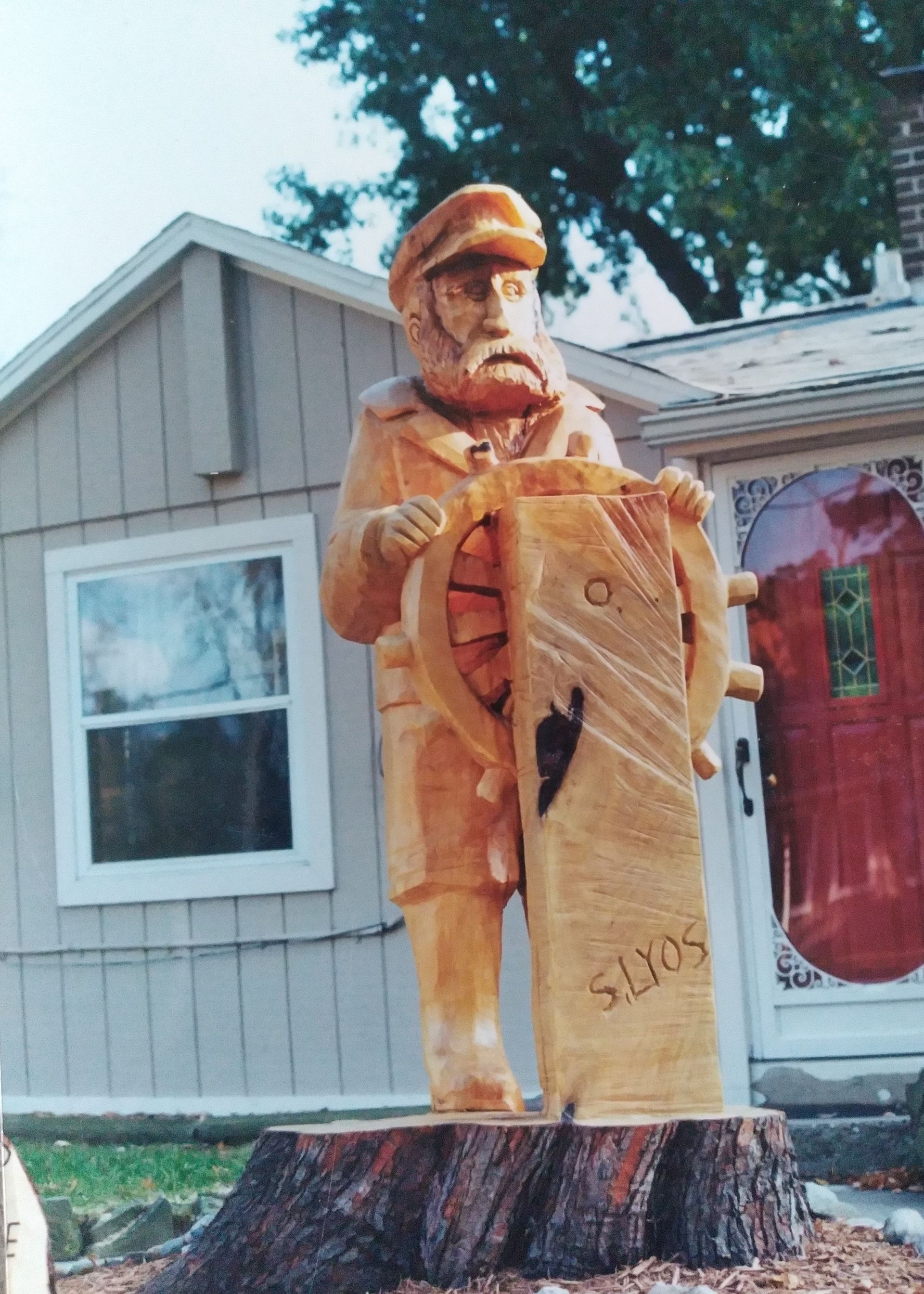 Carved wooden lumberjack statue beside a house, holding a chainsaw and standing on a tree stump.