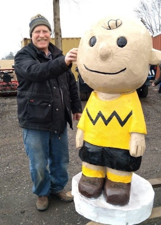 Man standing beside a large Charlie Brown statue outdoors, both smiling.