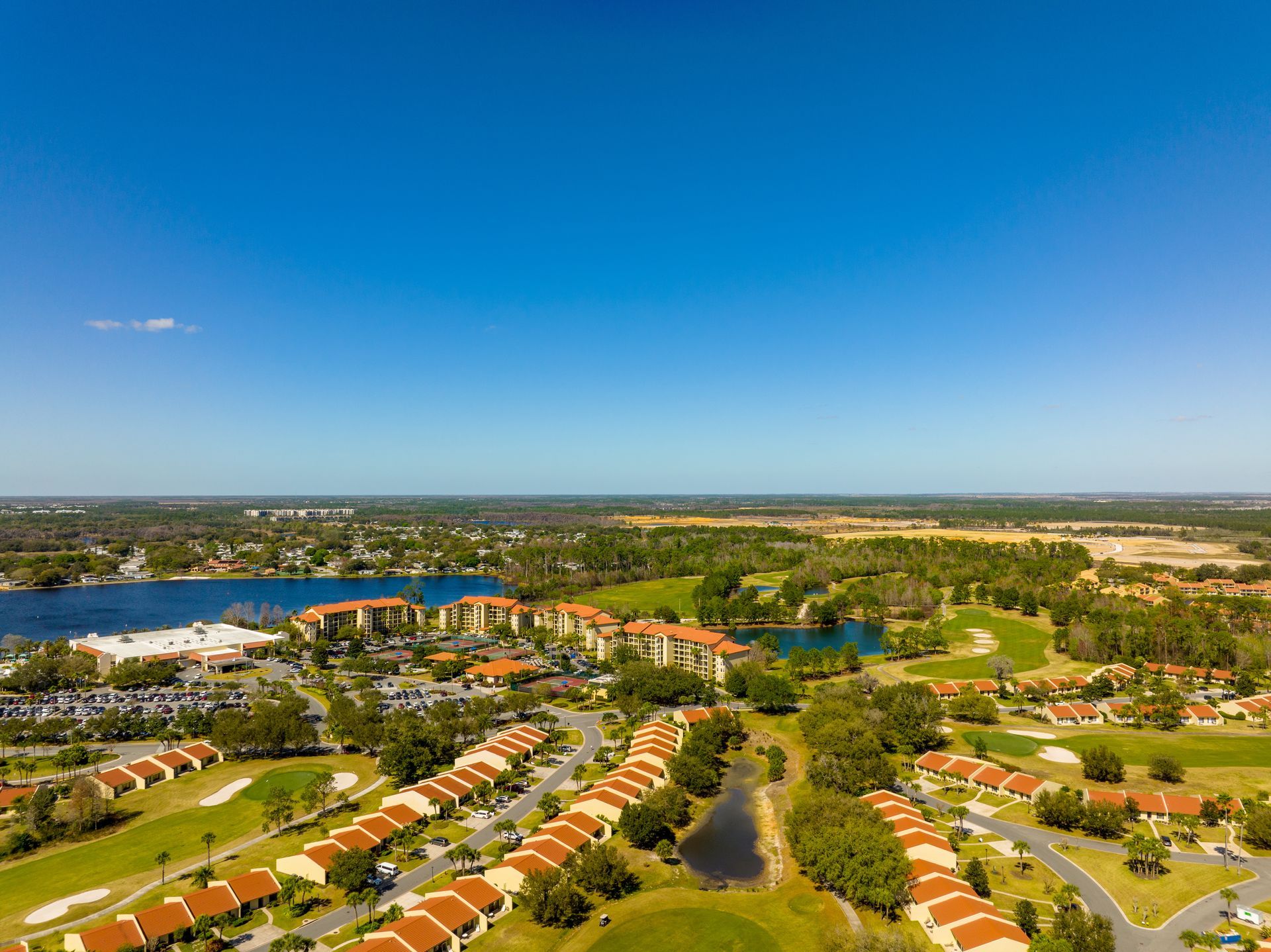 Aerial view of a suburban neighborhood with red-roofed houses, ponds, and a lake under a clear blue sky Aerial view of a suburban neighborhood with red-roofed houses, ponds, and a lake under a clear blue sky