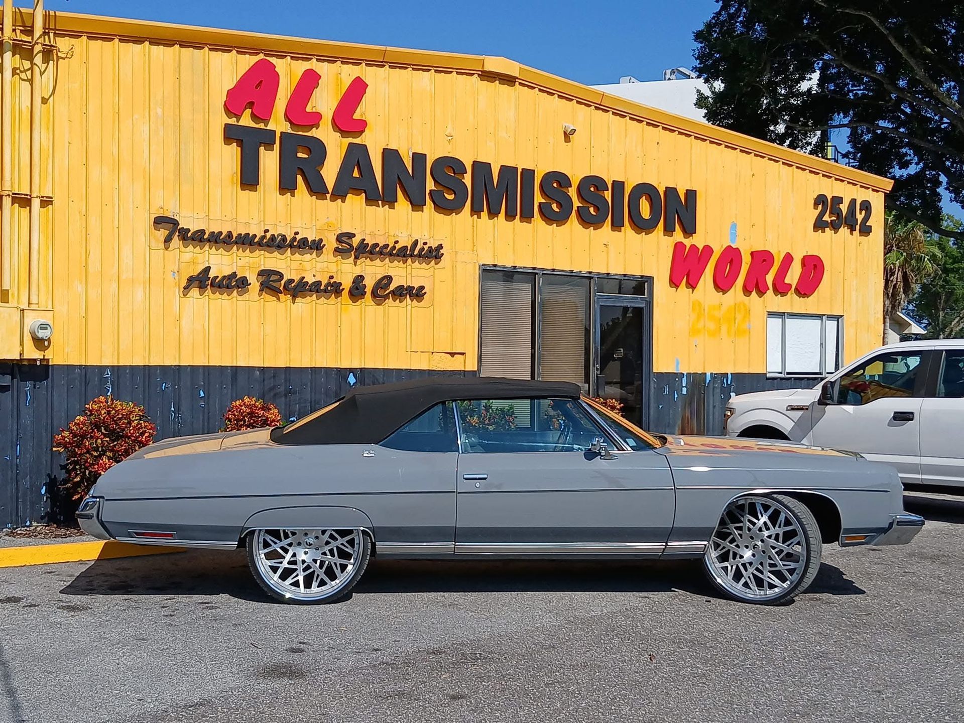 Gray classic coupe parked in front of the yellow All Transmission World shop