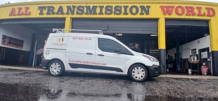 White service van parked outside All Transmission World auto shop under yellow/red signage