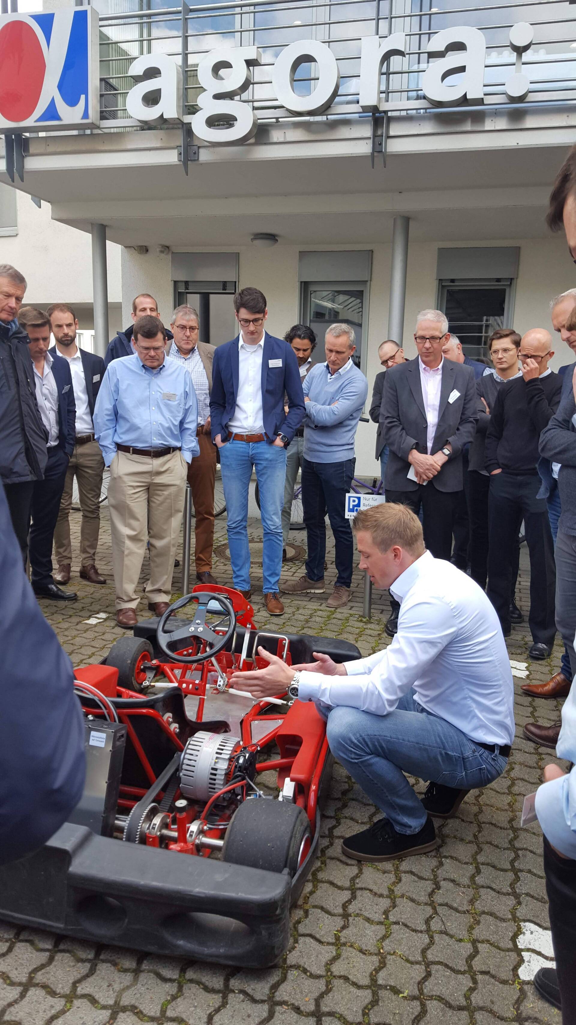 A group of men are looking at a go kart in front of a building.