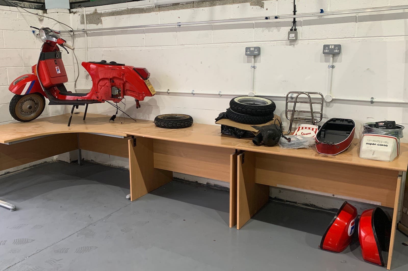 A red scooter is parked next to a wooden desk in a garage.