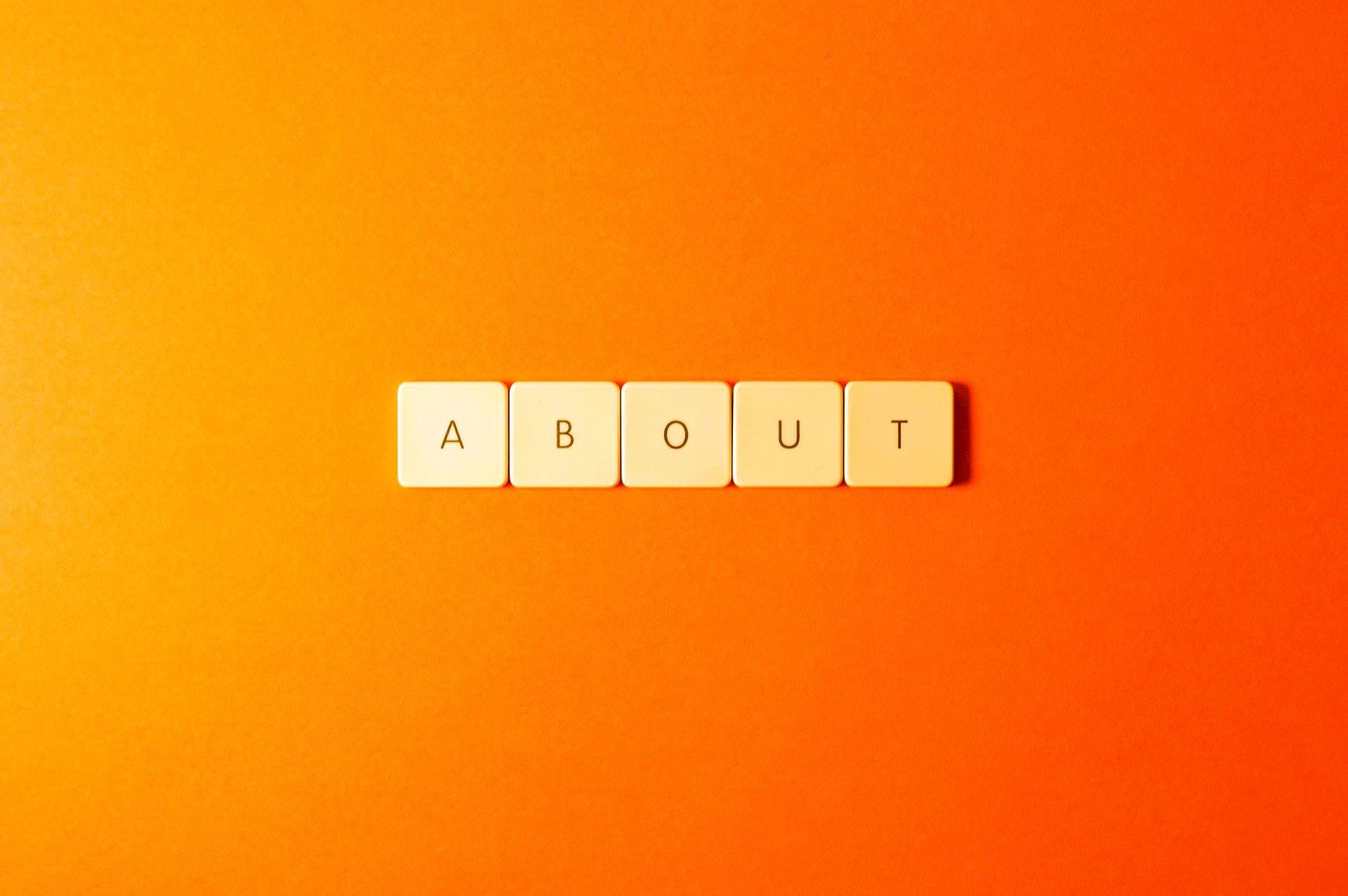 The word about is written in scrabble tiles on an orange background.