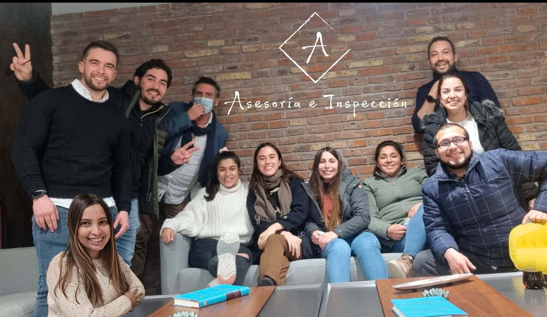 Un grupo de personas sonríen y posan en las escaleras de una habitación con paredes de ladrillo y una pizarra detrás de ellos.