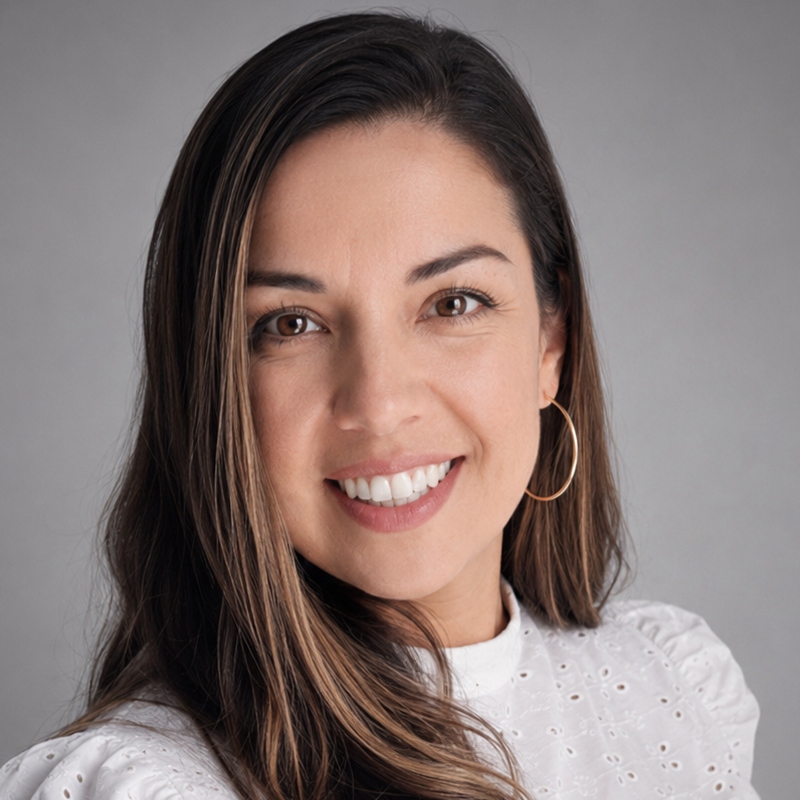 Mujer sonriente con cabello largo y oscuro que lleva una blusa blanca sobre un fondo gris.