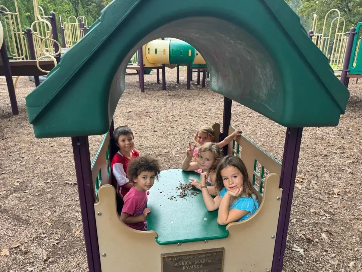 Children gathered around a table under a green playground canopy at a park
