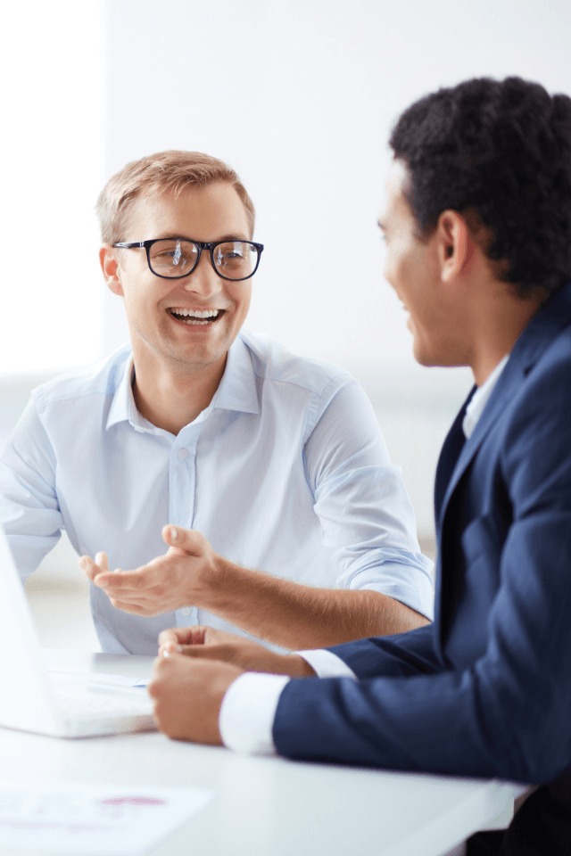 Two men are sitting at a table talking to each other.