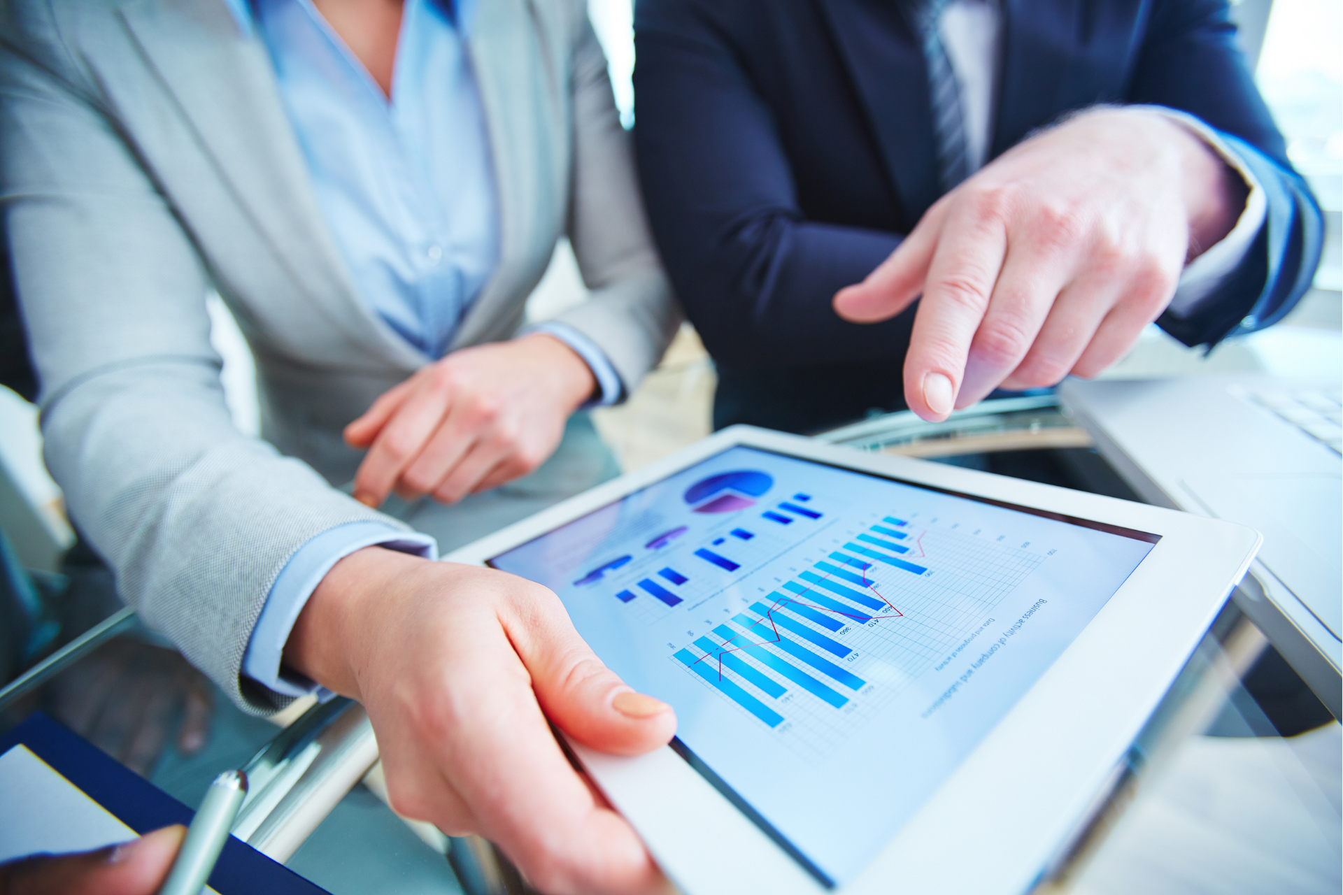 A man and a woman are looking at a tablet with a graph on it.