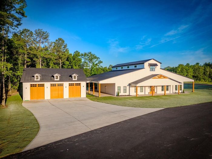 A large white barn with three garage doors is sitting on top of a lush green field.