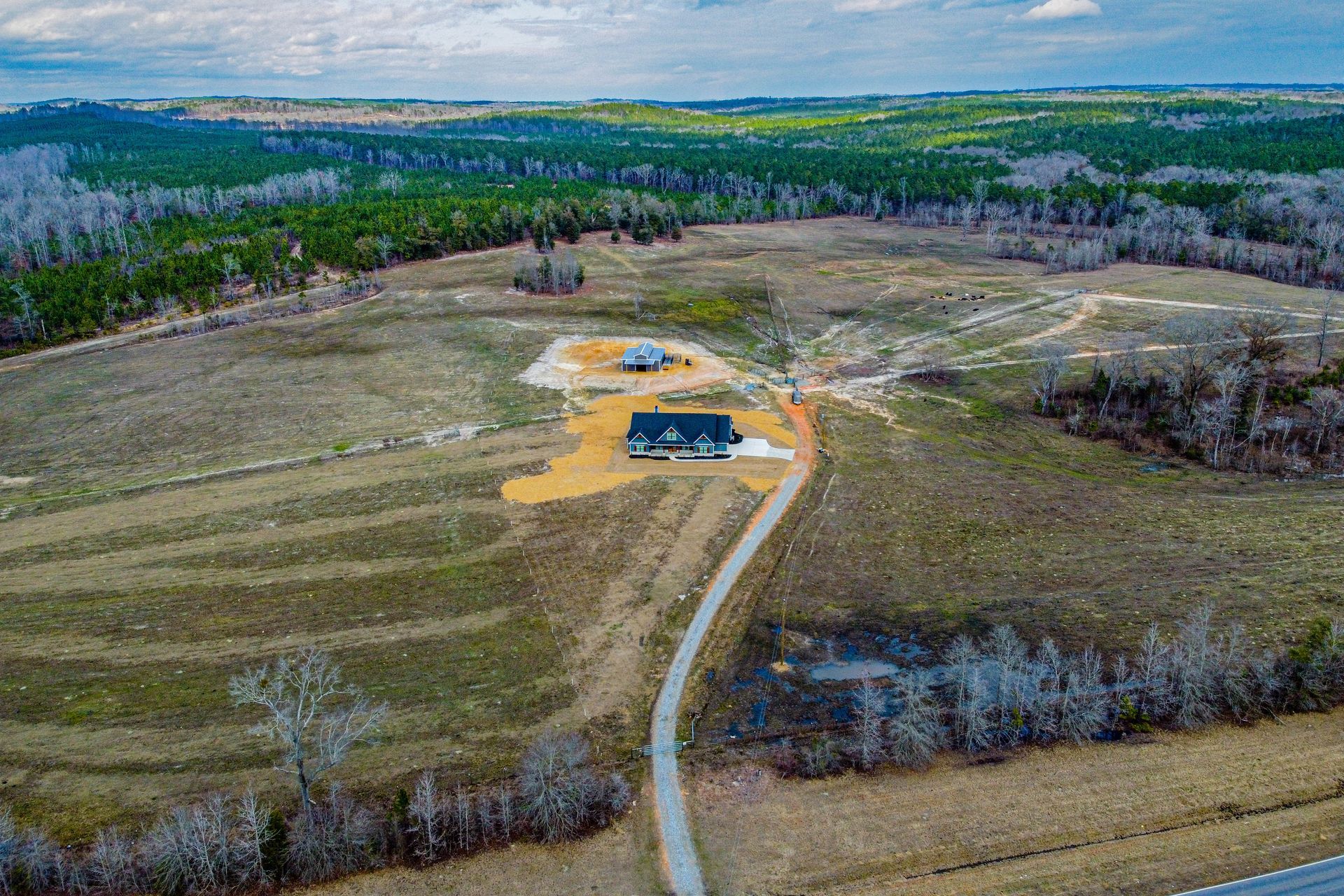 An aerial view of a house in the middle of a field surrounded by trees.