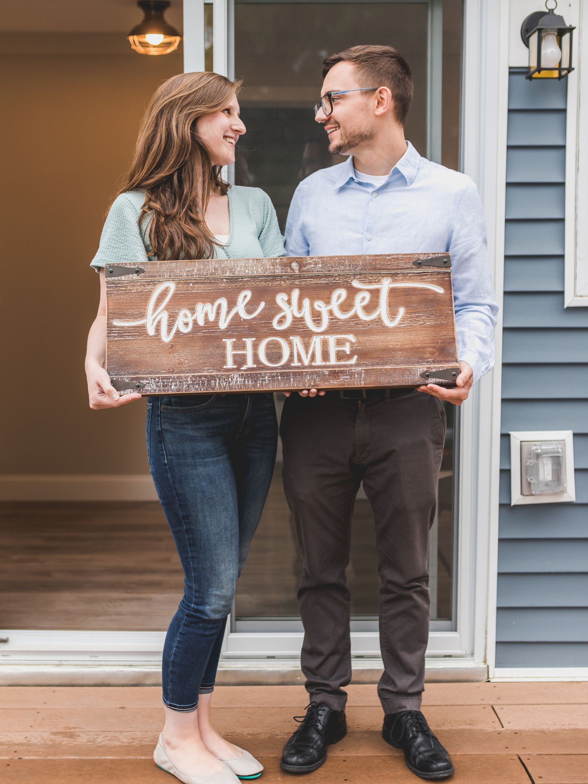A man and a woman are holding a sign that says `` home sweet home ''.