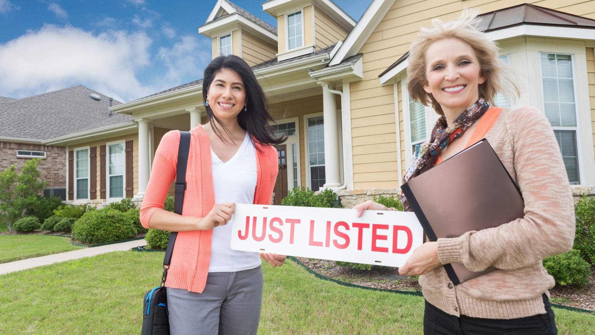 Two women are holding a just listed sign in front of a house.
