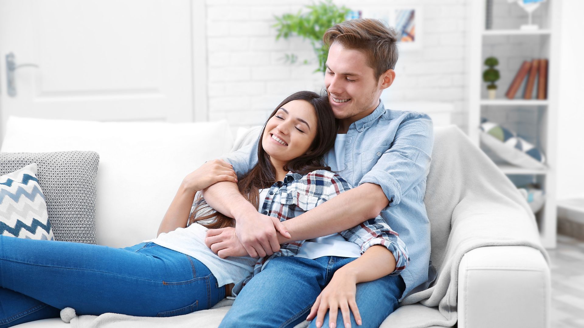 A man and a woman are sitting on a couch hugging each other.