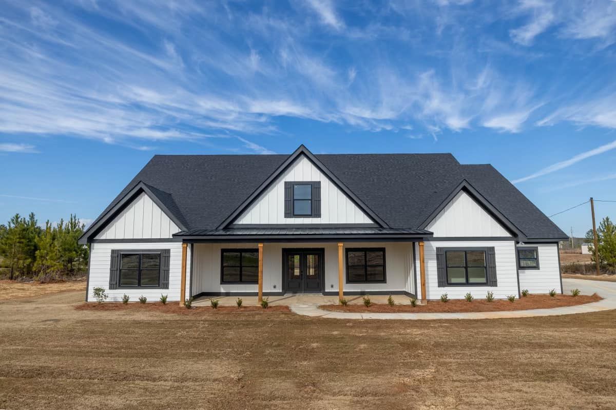 A large white house with a black roof is sitting on top of a dirt field.