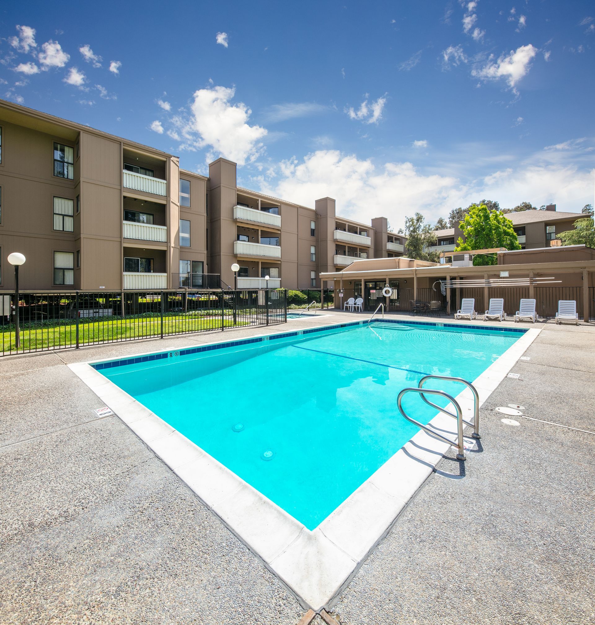 Outdoor apartment complex pool with turquoise water, metal handrails, and lounge chairs under a sunny blue sky at Vera West Valley in San Jose, CA.