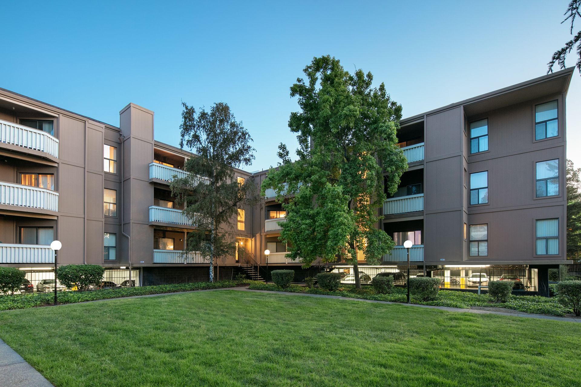 Apartment complex with brown buildings surrounding a grassy courtyard at dusk at Vera West Valley in San Jose, CA.