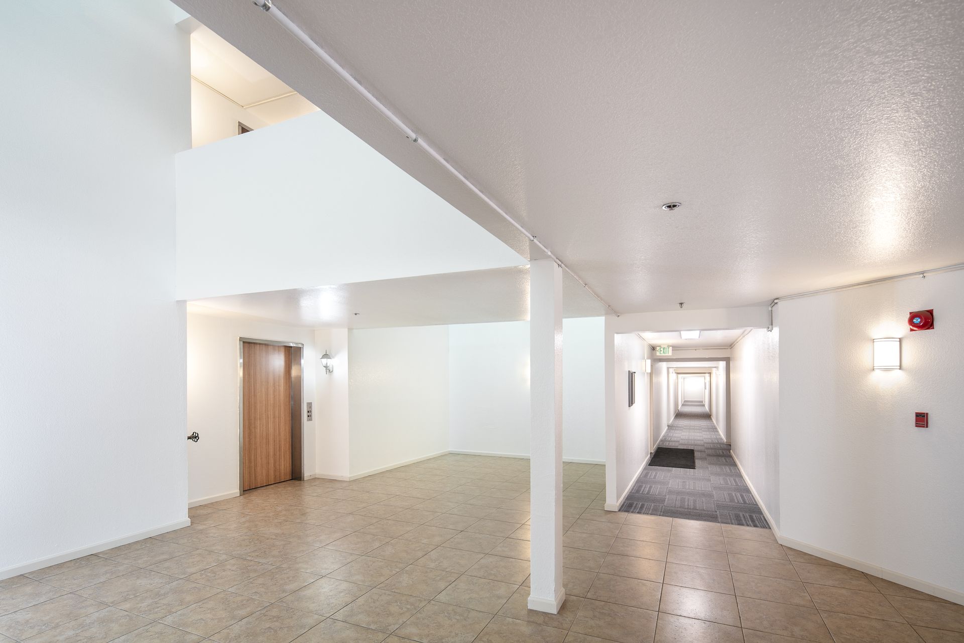 Bright white apartment hallway with beige floor, doors, and a long corridor leading to a distant window at Vera West Valley in San Jose, CA.