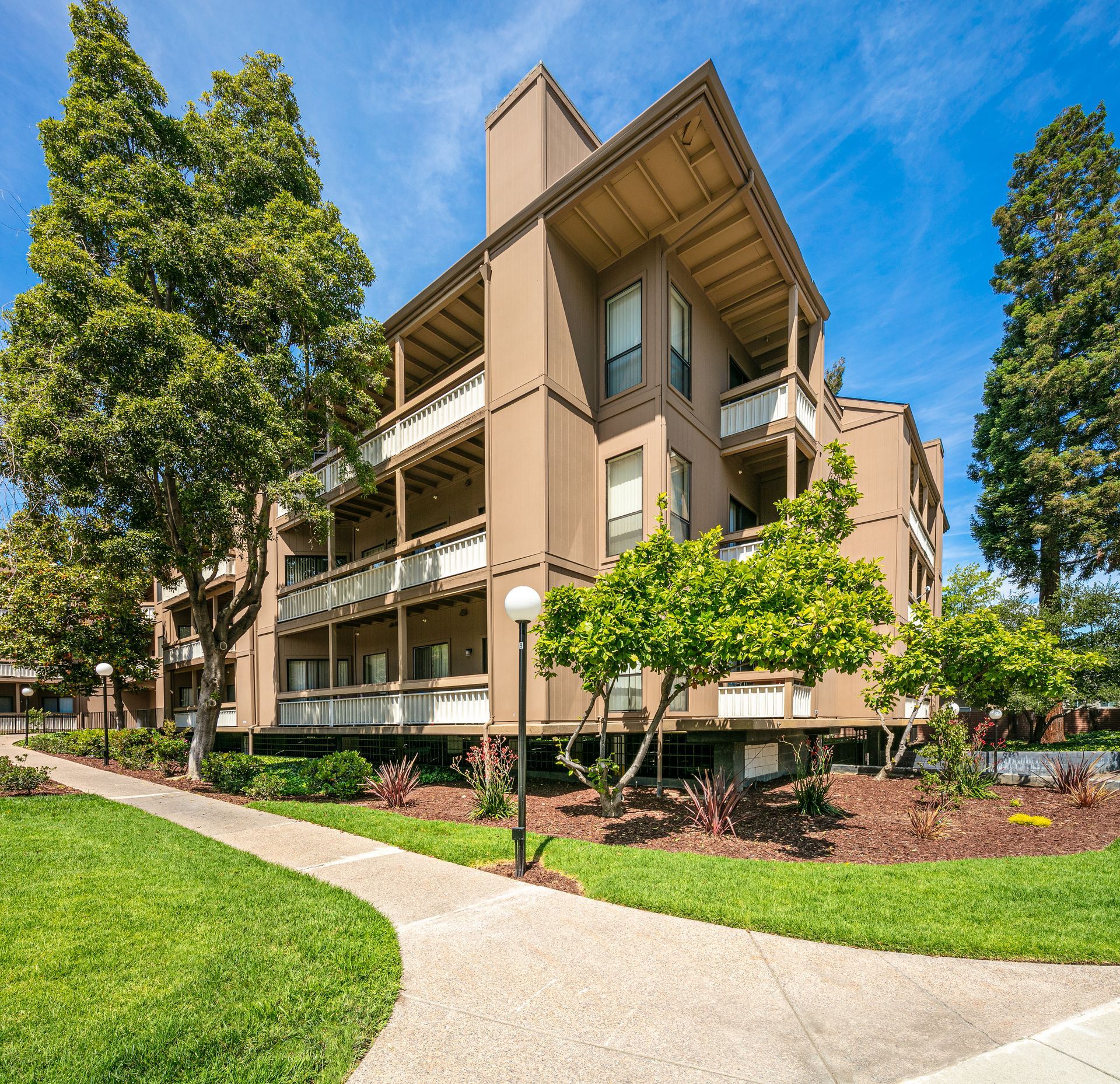 Modern apartment building with balconies, trees, and a winding sidewalk on a sunny day at Vera West Valley in San Jose, CA.