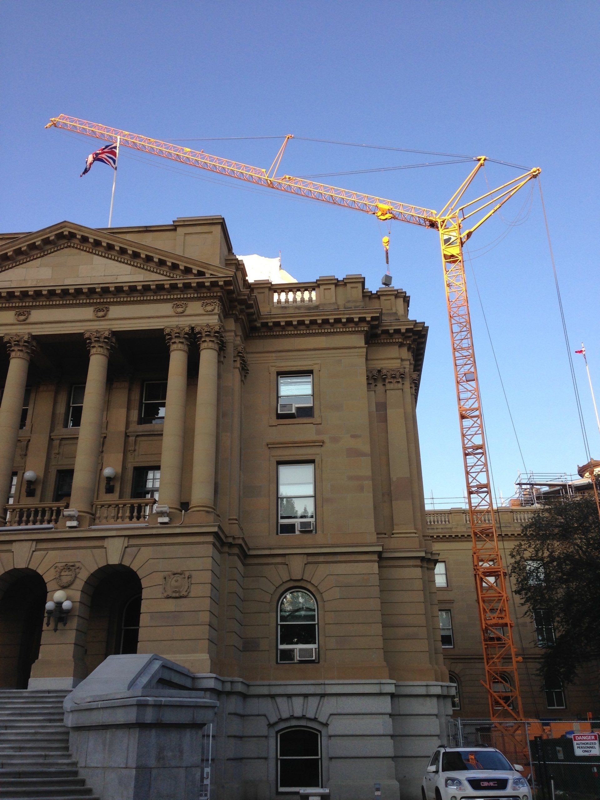 Construction crane next to a stone building with columns; blue sky.