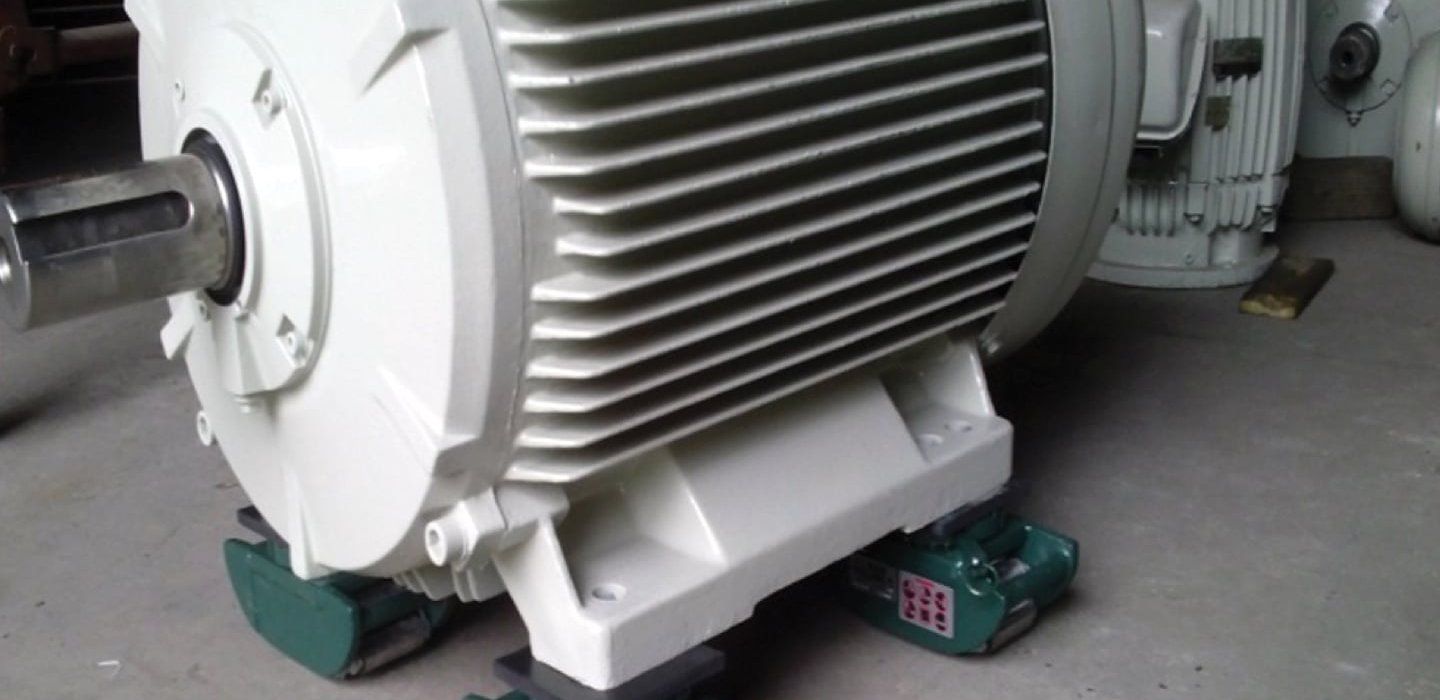 A large white industrial motor sits on green blocks in a factory.