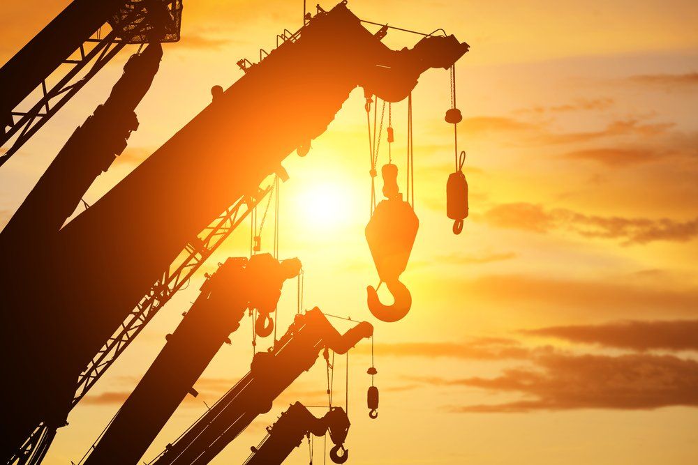 Silhouetted construction cranes against a bright sunset.