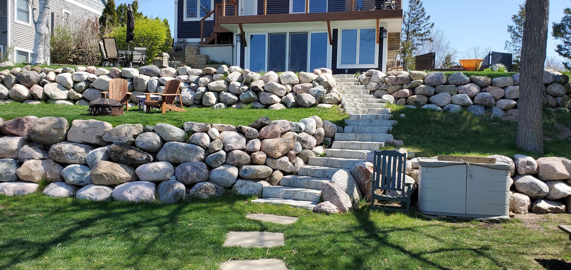 A house with stone walls and steps, overlooking a grassy area and lake.
