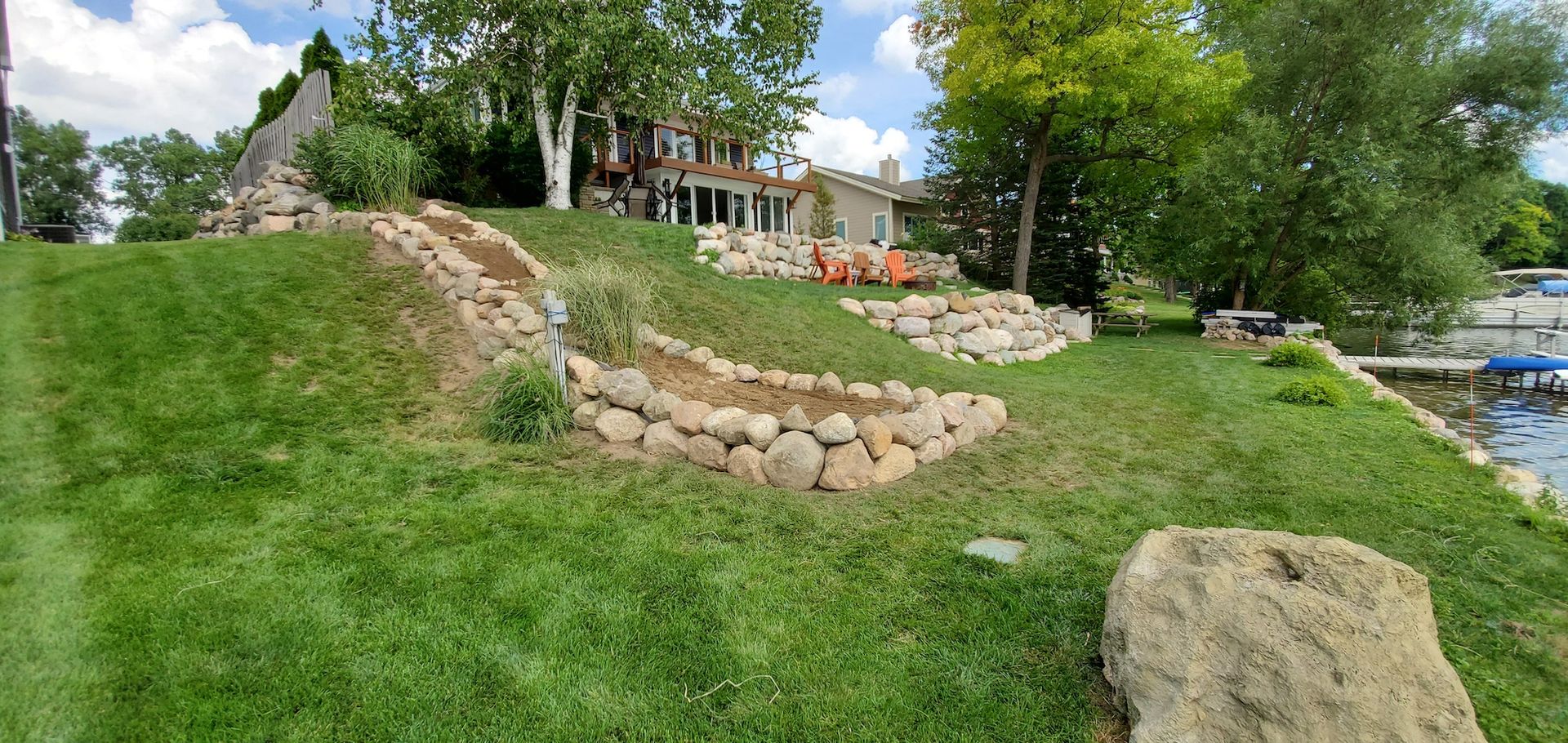 Green grassy hillside with a house, trees, and a stone retaining wall.