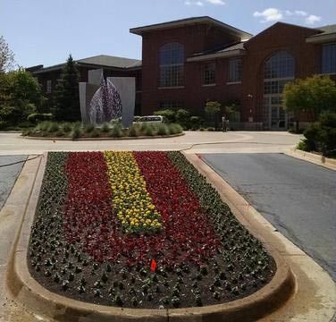 A colorful flower bed in front of a brick building. The flowers are arranged in stripes of red, yellow, and green.