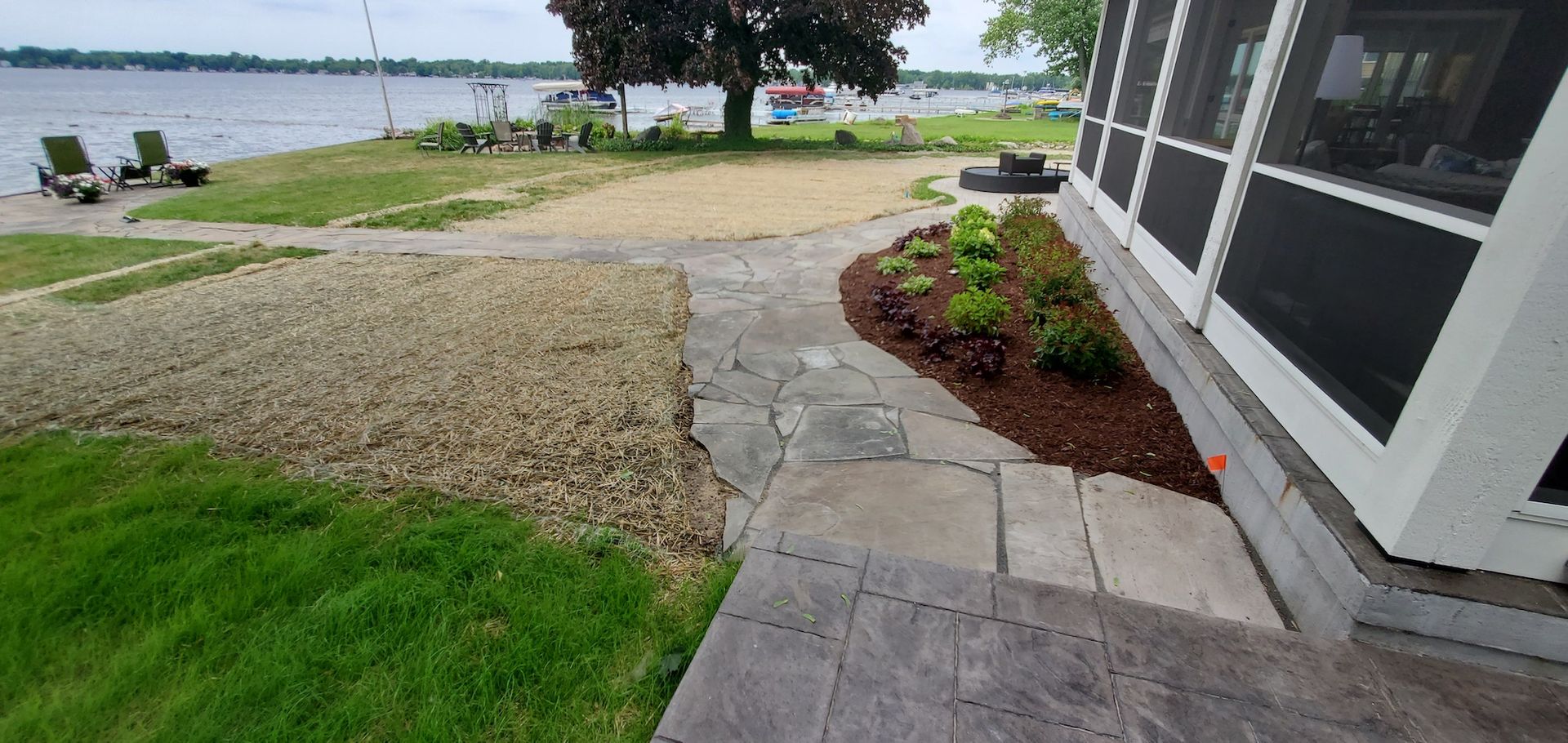 Stone walkway next to a house with a lake view, landscaping with mulch and plants.