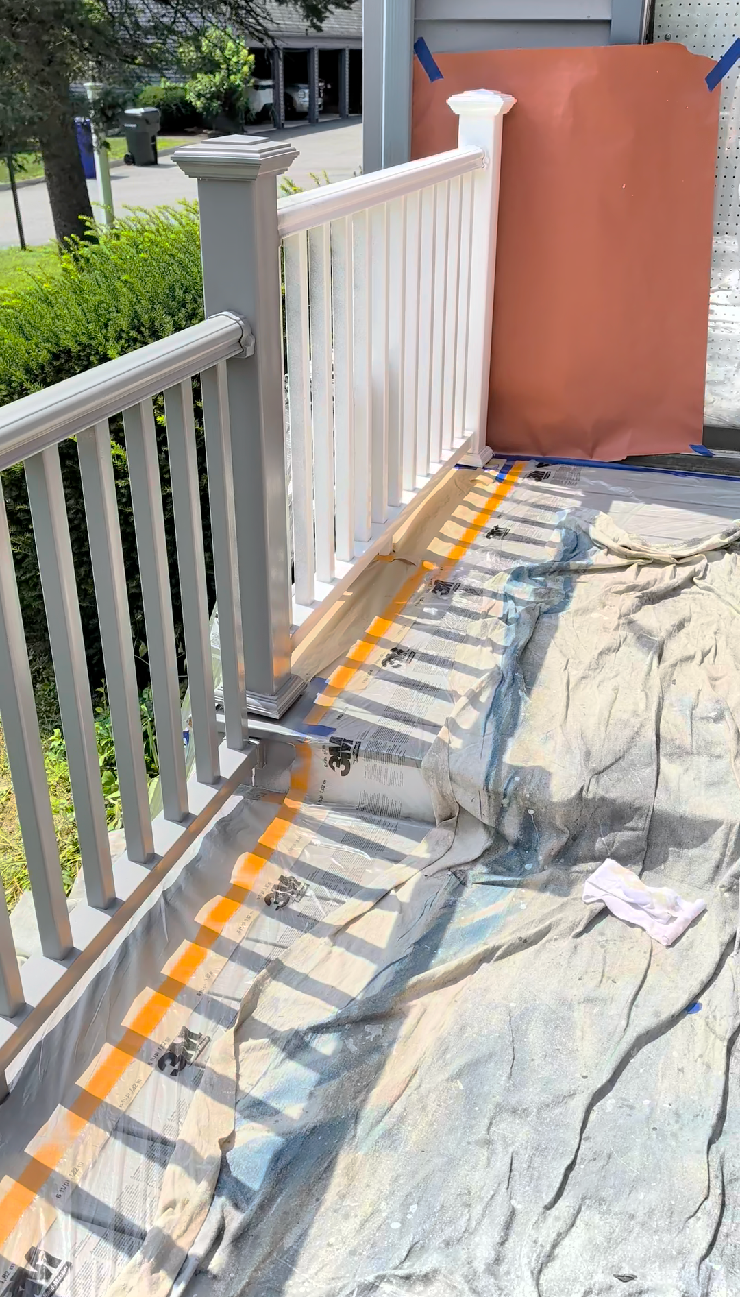 White porch railing with orange safety markings and a tarp-covered walkway beside a covered doorway