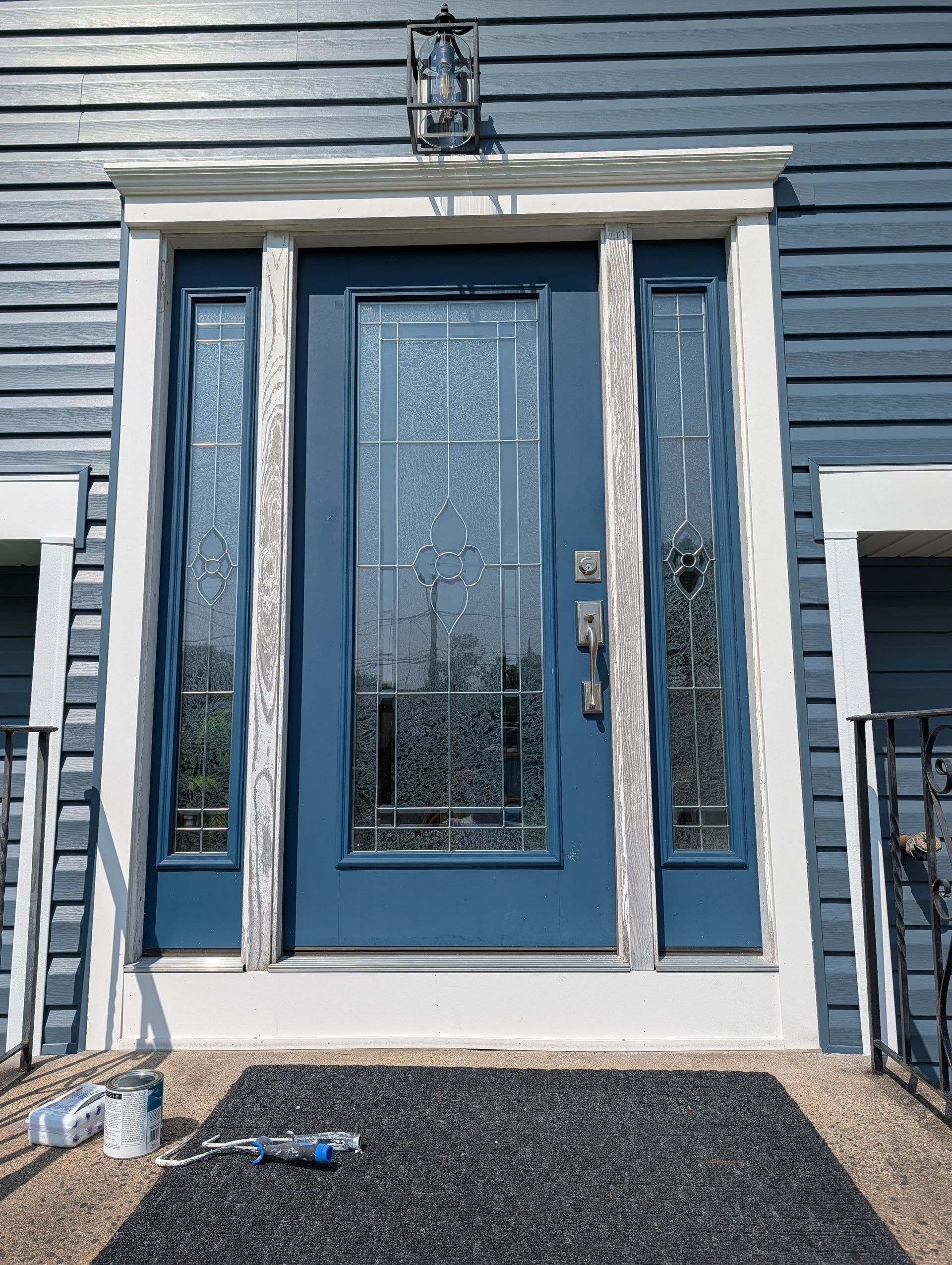 Blue front door with sidelights and white trim on a gray house exterior